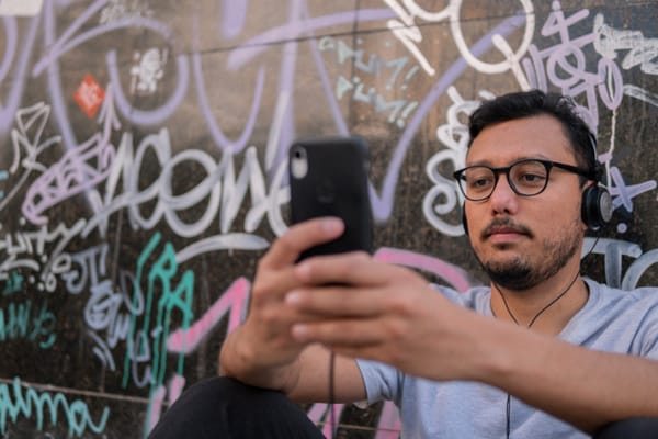 Homem sentado no chão com headphone na cabeça e celular nas mãos