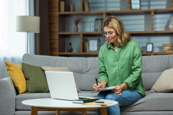 Mulher sentada no sofá fazendo anotações olhando para o notebook