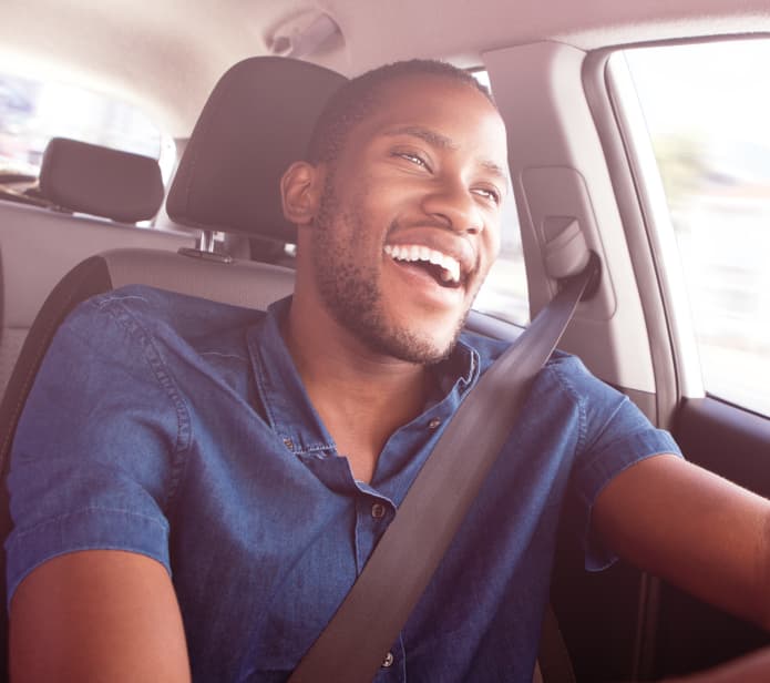 Imagem frontal de um homem dirigindo um carro olhando para a estrada e sorrindo.